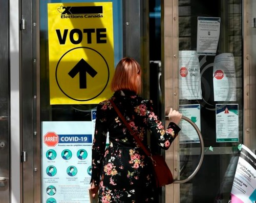 A person passes posters advising measures against COVID-19 as they enter Ottawa City Hall, a polling location, on election day during the 44th Canadian general election, on Monday, Sept. 20, 2021. The Liberals and New Democrats have been declared the winners in two hotly contested British Columbia federal ridings too close to call on election night. THE CANADIAN PRESS/Justin Tang