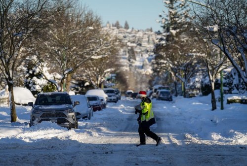 A Canada Post letter carrier crosses a snow-and-ice covered road while delivering mail in Burnaby, B.C., on Wednesday, Dec. 21, 2022. A snowstorm dumped more than 30 centimetres of snow in Metro Vancouver this week. THE CANADIAN PRESS/Darryl Dyck