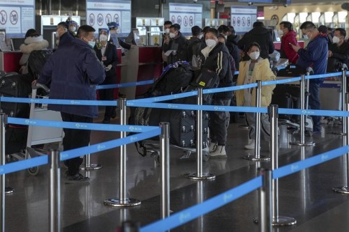 Masked travellers with luggage line up at the international flight check in counter at the Beijing Capital International Airport in Beijing, Thursday, Dec. 29, 2022. An expert says Canada's requirement of a negative COVID-19 test of travellers from China will not help in preventing new variants or the spread of the virus. THE CANADIAN PRESS/AP/Andy Wong