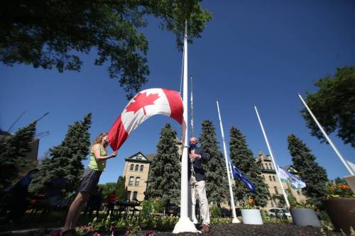 Brandon University president David Docherty (right) raises the Canadian flag in front of BU along 18th Street. Docherty says being a citizen means 